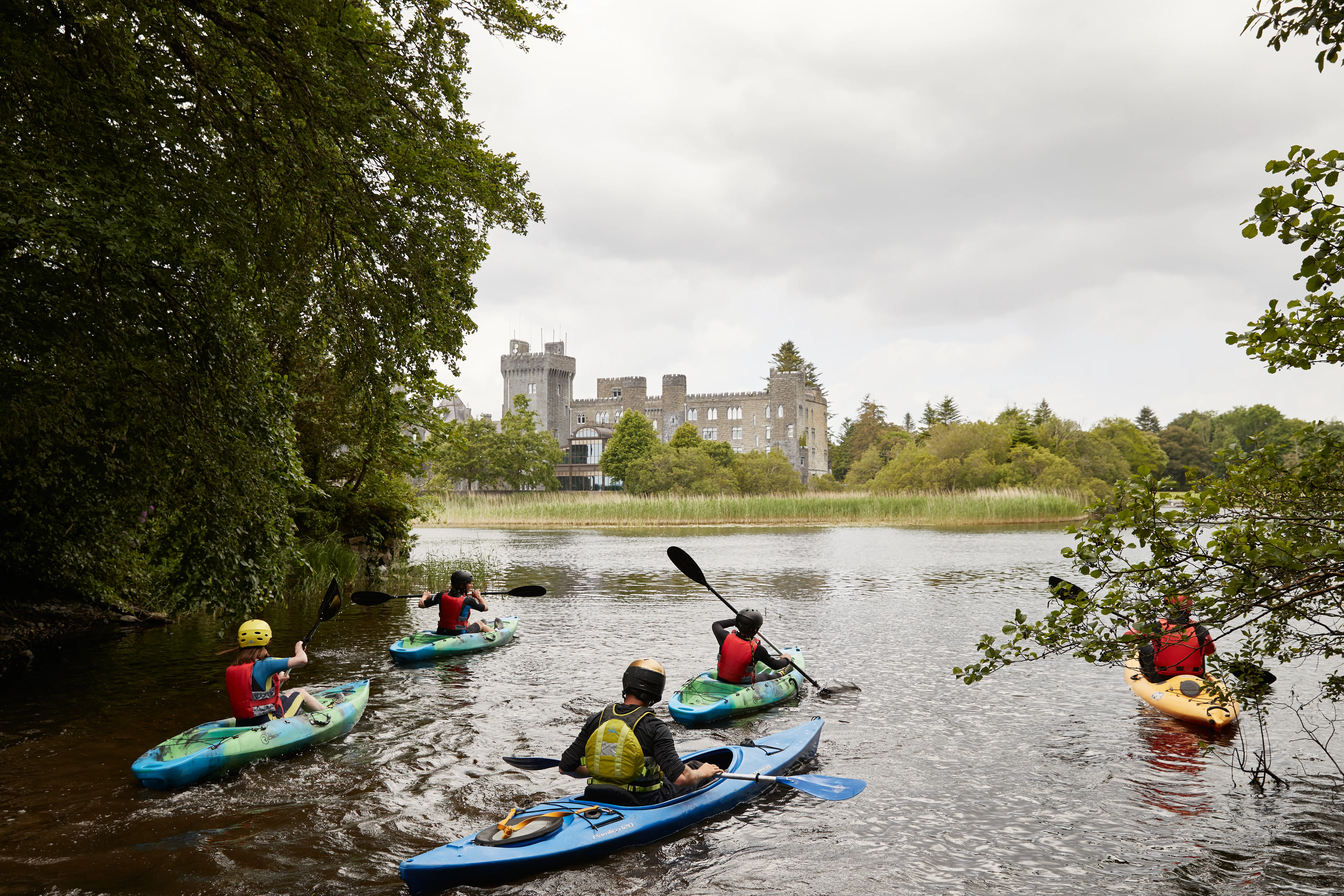 Kayakers on the Cong River with Ashford Castle towers visible through the trees