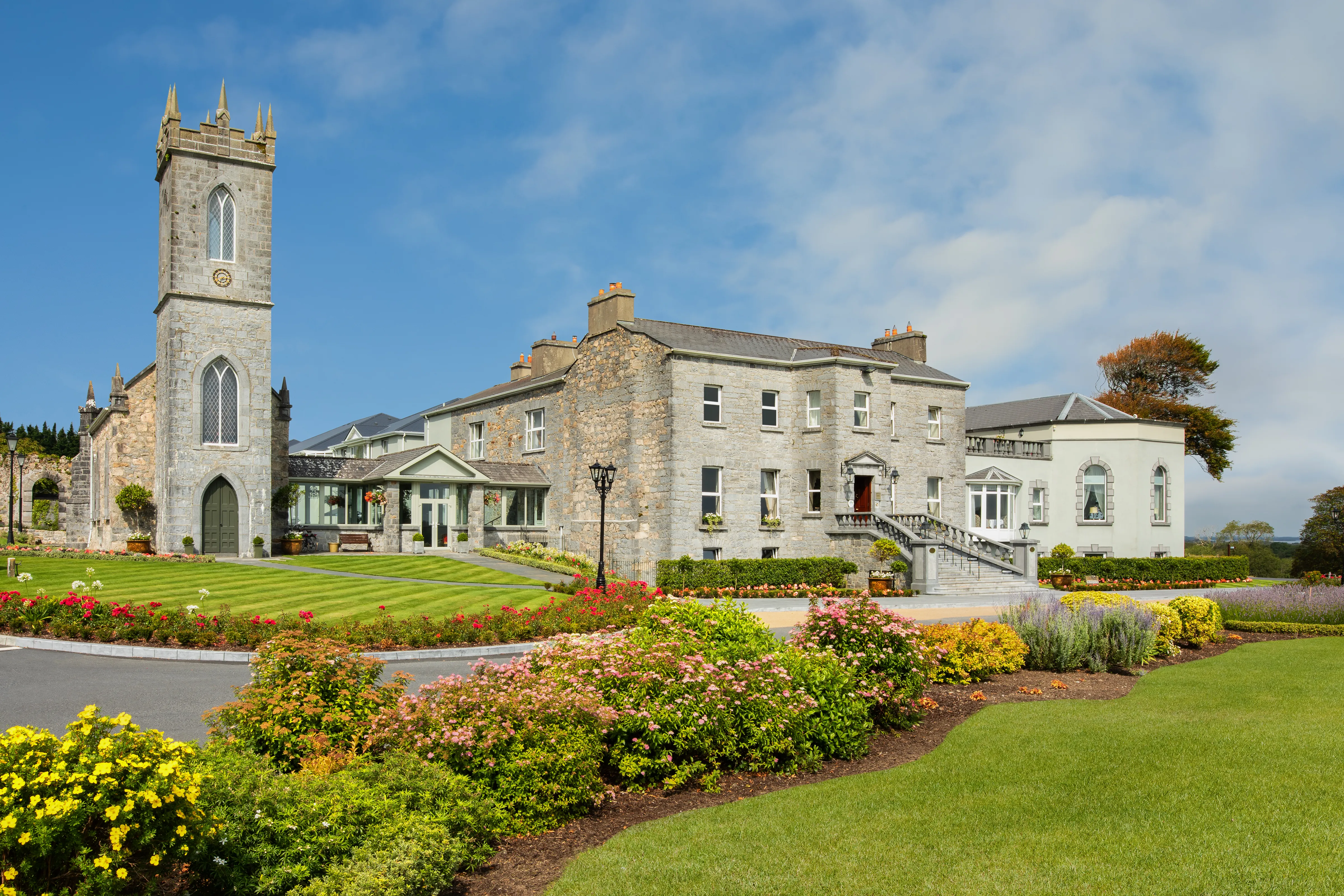 Glenlo Abbey Hotel facade with church tower, parterre gardens and blue sky
